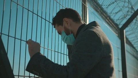 Sad man wearing Protective Face Mask stand near fence border look around COVID Stock Footage 126585554