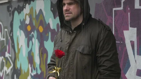 Sad man with wet jacket holding red rose and waiting woman on downpour, tilt up. Stock-Footage 61130897