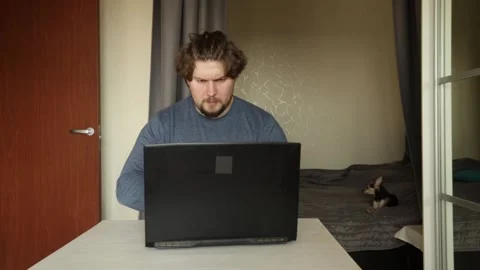 Sad man working on laptop, typing at a modern desk indoors, showing signs o.. Stock Footage 297664433