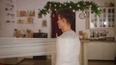 Sad man wrapping himself in stretch cellophane on Christmas Eve Stock Footage 168871322