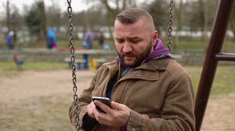 Sad man writing a message and sitting at the swing and swinging  Stock Footage 60962757
