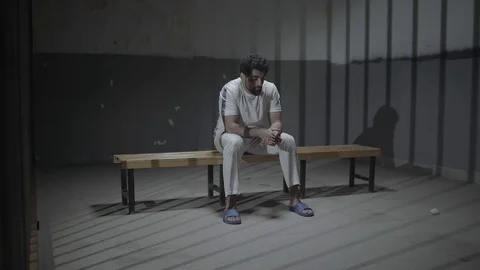 A sad oppressed young man sitting in prison room Vidéo 106822984