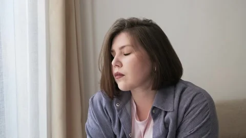 Sad plump or overweight young girl looks out window portrait. Problems of Stock-Footage 248674493