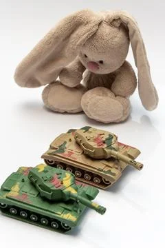 Sad plush bunny looking down at two toy tanks isolated Stock Photos