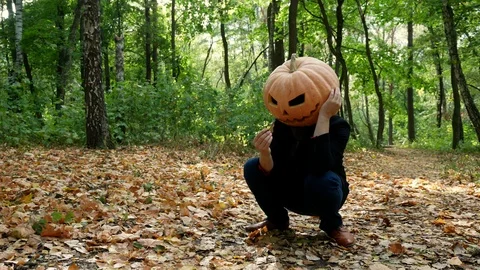 Sad pumpkin-headed man sitting on the ground in the autumn forest. Halloween Video stock 116493113