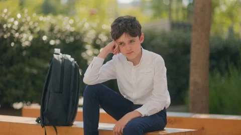 Sad schoolboy sitting alone on a bench in schoolyard during break time Stock Footage 310016696