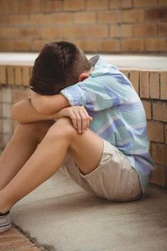 Sad schoolboy sitting alone on steps in campus Foto stock