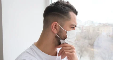 Sad serious man in self isolation wearing face mask looking at the window Stock Footage 150022442