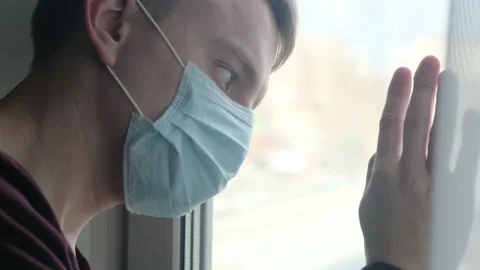 Sad sick man in a mask looking out the window. Coronavirus Isolation Stock Footage 126342609