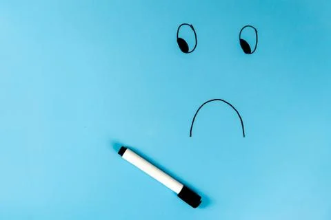 A sad smiley is drawn with a marker on a blue background. Free space for text Stock-Fotos