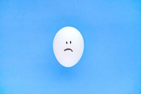 Sad smiley face on an isolated egg on a blue background. Close up. Foto stock