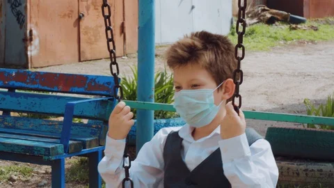 Sad student in protective mask on a swing, hold rusty metal chains on sunny day Video stock 127832176