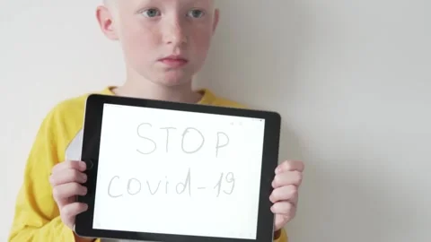 A sad teenage boy holds a tablet with the inscription on the screen STOP COVID Stock Footage