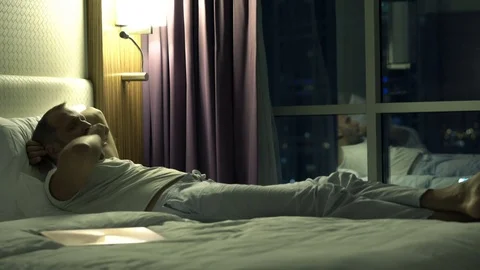 Sad, unhappy man lying on bed during night Stock Footage 83312853