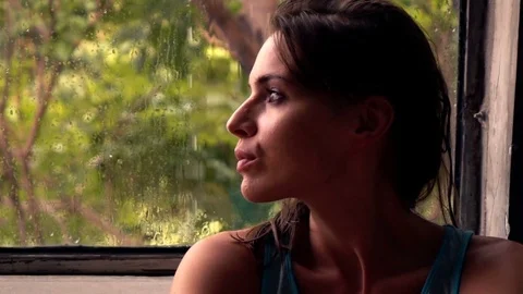 Sad, unhappy woman looking by window at home during rain, super slow motion Stock Footage