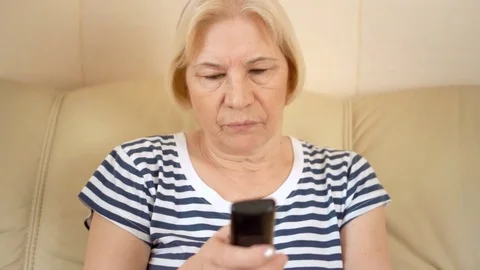 Sad upset good-looking senior woman sitting on sofa at home. Talking with friend Stock Footage 74433117
