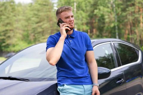 Sad upset guy driver is standing near broken car after road accident, crash Stock Photos