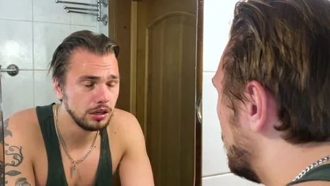 Sad white man crying in front of the mirror, feeling miserable and broken inside 스톡 동영상 194176807