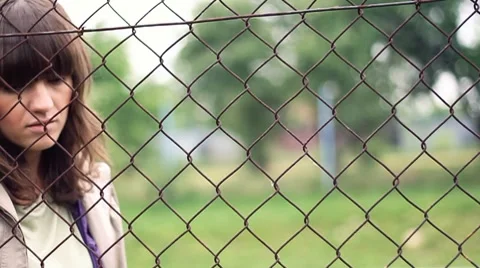 Sad woman behind chain-link fence, outdoors, dolly shot HD Stock Footage