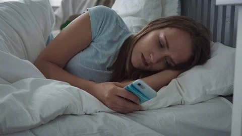 Sad woman lying on bed using smartphone and trying to fall asleep Stock Footage 93246430