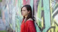 sad woman with a red shirt is crying leaning against a wall painted with murals HD Footage
