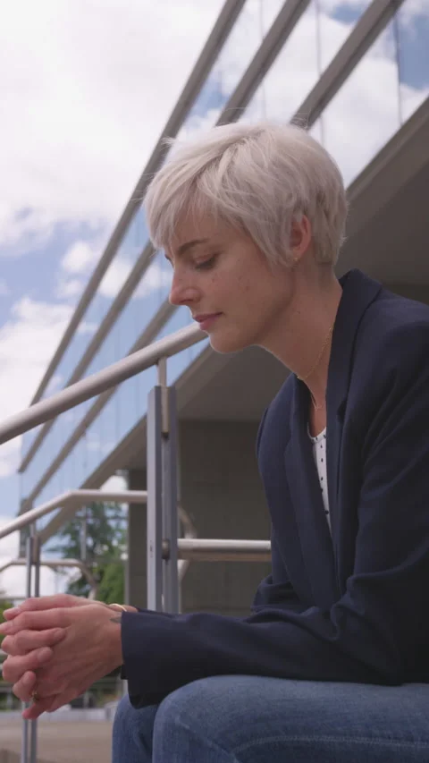 Sad Woman with Short Pixie Cut Sitting near Downtown Building in Natural Light Stock Footage 208778176