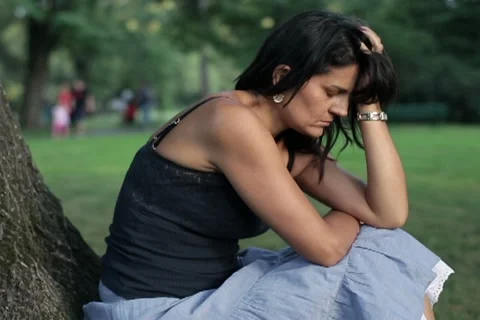 Sad woman sitting in the park under tree Stock Footage