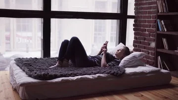 Sad woman using smartphone, lying on bed by window, overlooking city street Stock Footage 86086155