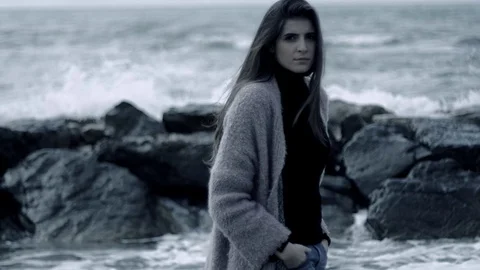 Sad woman walking in front of wild ocean big waves looking camera Stock Footage