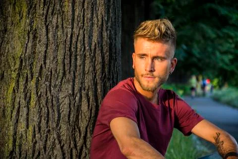 Sad, worried blond young man against tree Stock Photos