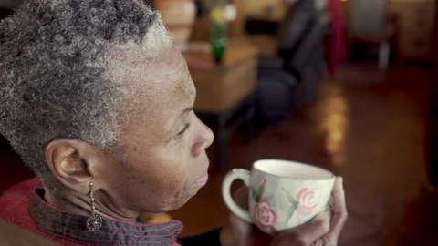 Sad, worried, senior black woman holding a hot beverage in a rocking chair Stock Footage