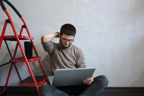 Sad young bearded hipster using laptop, on white background near red metallic Stock-Fotos