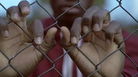 Sad young black african migrant behind prison net.Illegal immigration Stock Footage