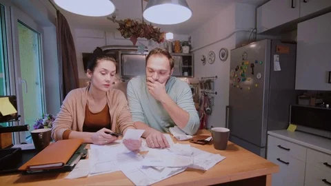 Sad young couple paying the bills. Man and woman sitting in the kitchen and Stock Footage