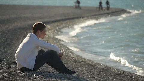 Sad Young guy sitting on the beach, covering his face with his hands Stock Footage 114157999