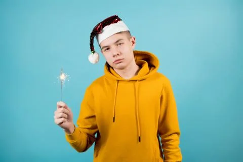 A sad young guy without mood holds a burning sparkler in his hand on a blue Stock Photos