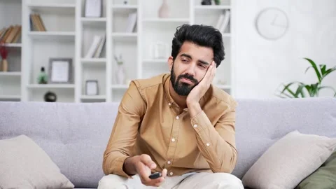 Sad young handsome bearded man bored switching television channels  Stock Footage 252216119