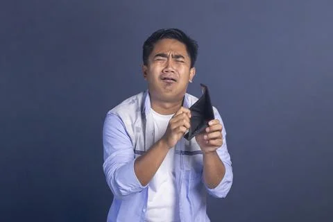 Sad young man crying while looking at his empty black wallet against a dark.. Stock Photos