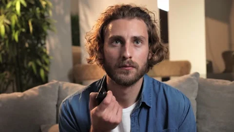 Sad young man holds a remote control in his hands and switches channels on TV. Video stock 167218635