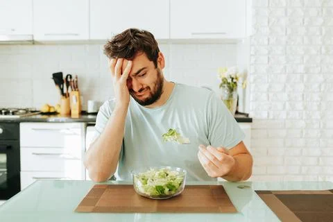 Sad young man look longingly at salad hold fork with greens in hand plate salad Stock Photos