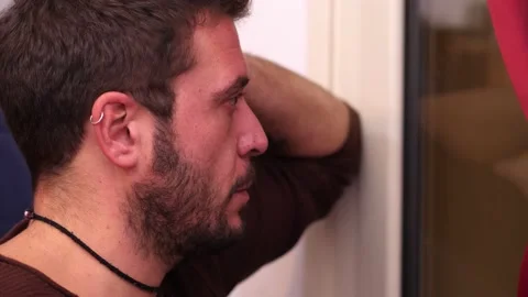 Sad young man looking out the window at home feeling depression Stock Footage 169527240