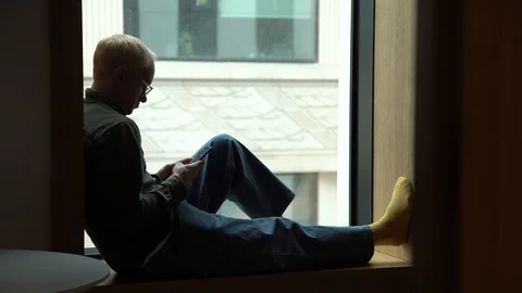Sad young man looks through window. Stop COVID-19 infection. Touch phone Stock Footage 129062157