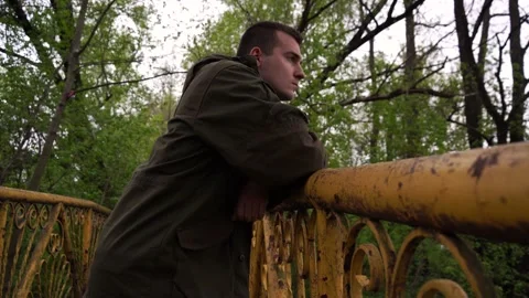 A sad young man with problems on a bridge by the river, close-up. Video stock 164303525