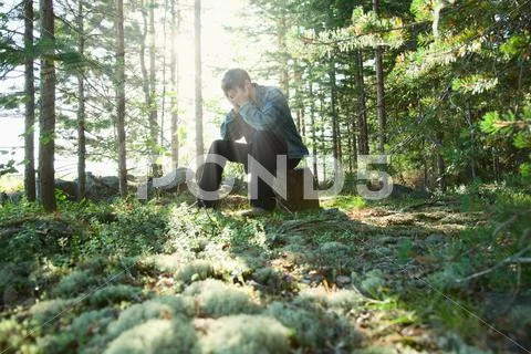 Sad young man sits in wood on stone Stock Photos