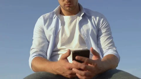 Sad young man sitting open-air and reading bad message on smartphone, break-up 動画素材 117194751