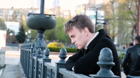 Sad young man standing leaning on a fence on the embankment on the bridge Stock Footage 106719734