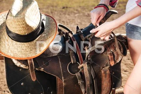 Saddle prepared for horse riding by young woman cowgirl Stock Photos
