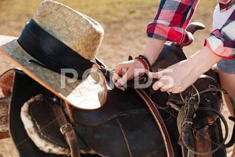 Saddle prepared for horse riding by young woman cowgirl Stock Photos