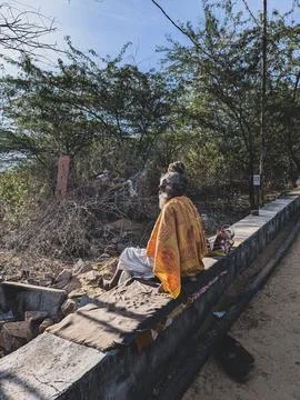 A sadhu wrapped in a yellow shawl sits quietly on a roadside wall in a rura.. Stock Photos