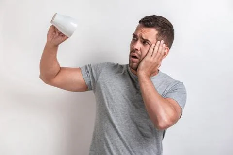 Sadly man flips an empty cup and looking unhappy, touches on cheek.- Image Stock Photos